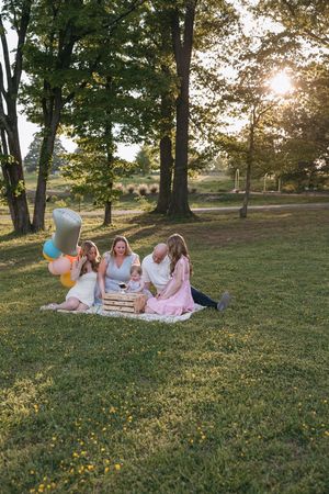 A group enjoys a picnic on a grassy hill at sunset with colorful balloons and a basket on their blanket.