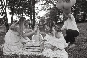 Black and white scene of children having a picnic celebration outdoors with balloons and presents on a summer day.