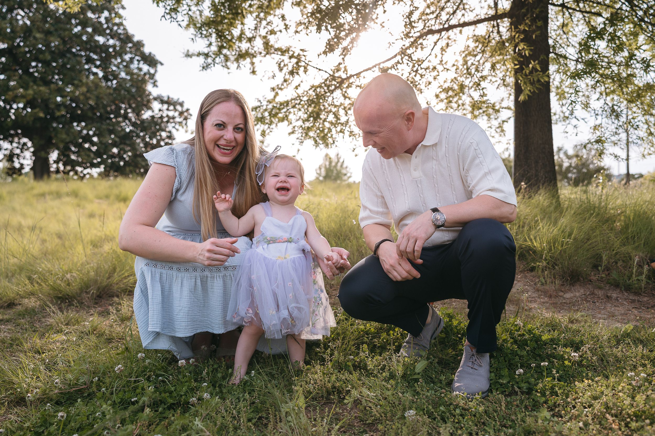 A family enjoying a sunny day together in a grassy field with trees in the background.