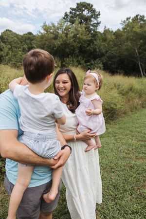 A family shares tender moments together while standing in a grassy field on a sunny afternoon.