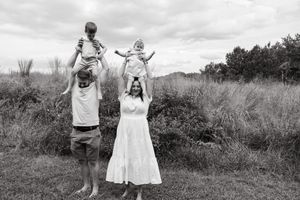 A joyful family moment captured in black and white as parents lift their young children on their shoulders in a grassy field.