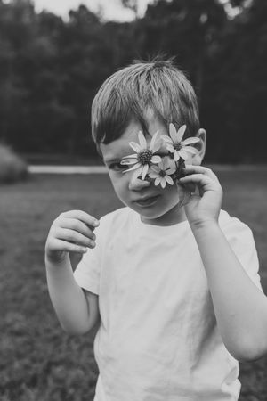 Black and white photo series shows a child playfully holding fresh daisies in front of their eyes.