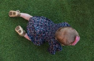 Baby in floral dress lying on artificial green turf.