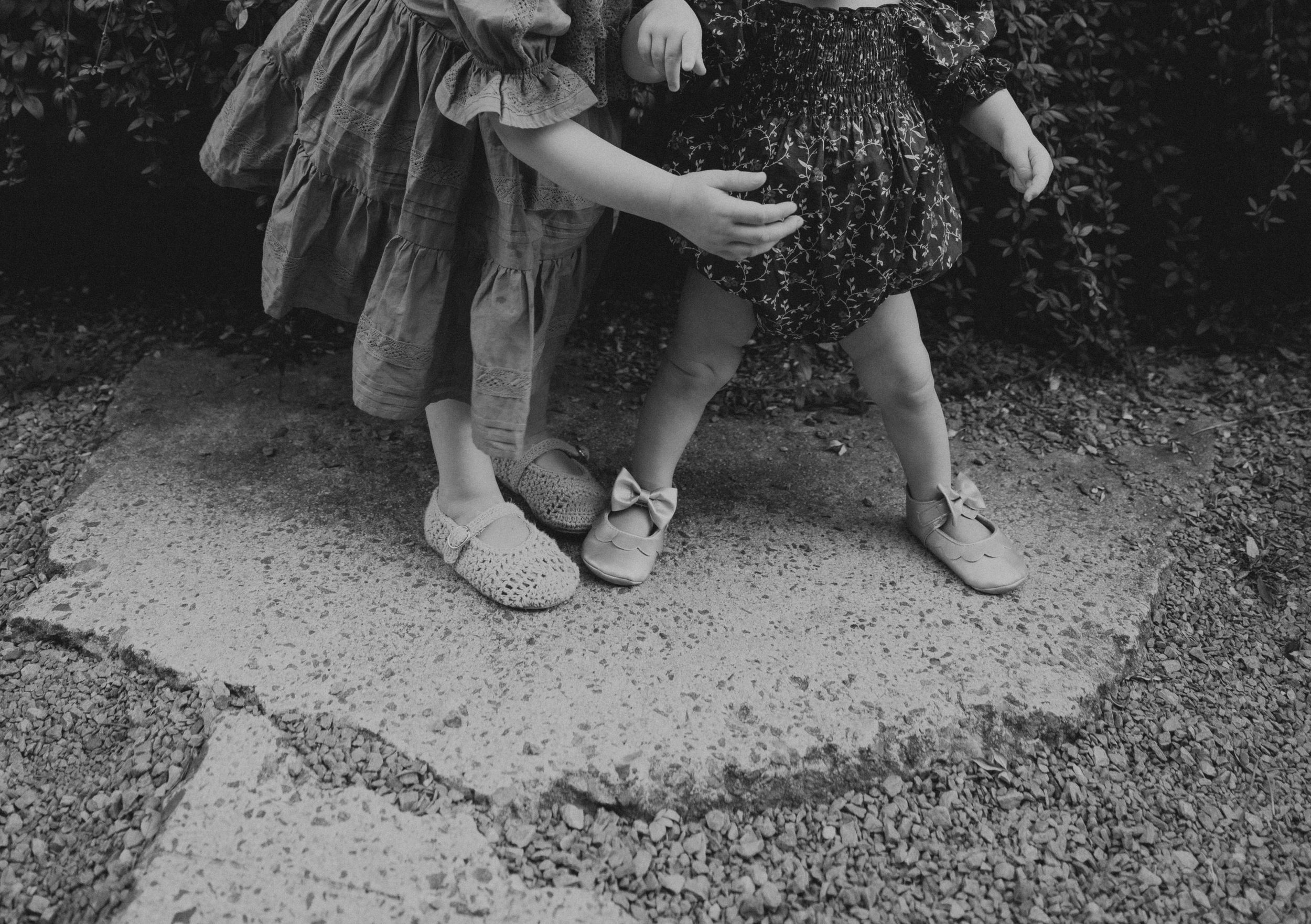 Black and white image of children's feet and shoes on pavement.