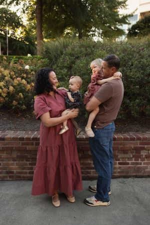 A family shares a joyful moment together on a brick-lined pathway near garden shrubs.
