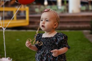 Child in a navy dress standing outdoors with colorful balloons.