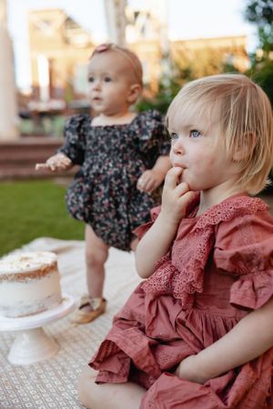 Two small children in dressy outfits looking intently during an outdoor celebration.