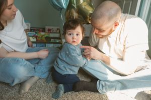 A young family sits on a carpet floor, with parents bonding with their curious toddler in a cozy, warmly lit room.