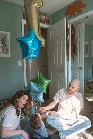 Family sitting on floor with colorful star-shaped balloons in a child's bedroom.