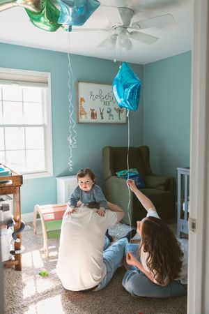 Parents playing with baby in teal nursery with blue star balloons and animal name sign on wall.