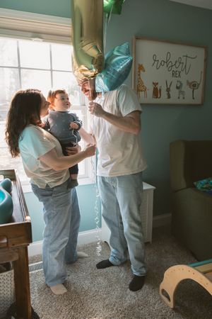Parents celebrate baby Robert Rex's first birthday in a teal nursery with balloon decorations.