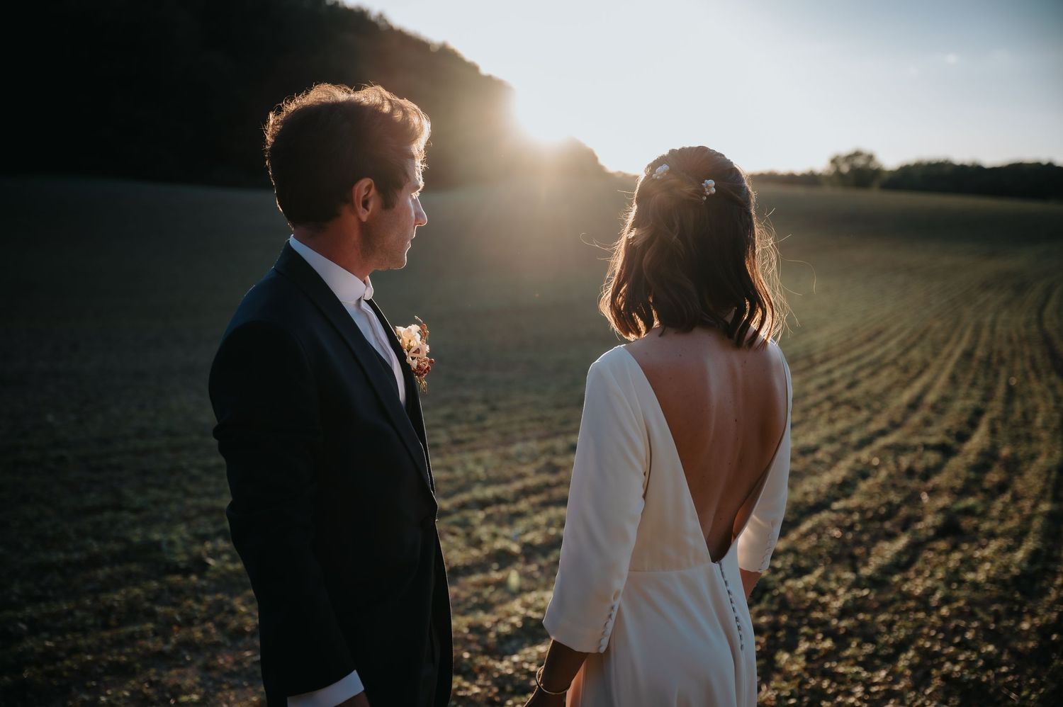 Romantic sunset photo of a couple in formal wear standing in an open field.