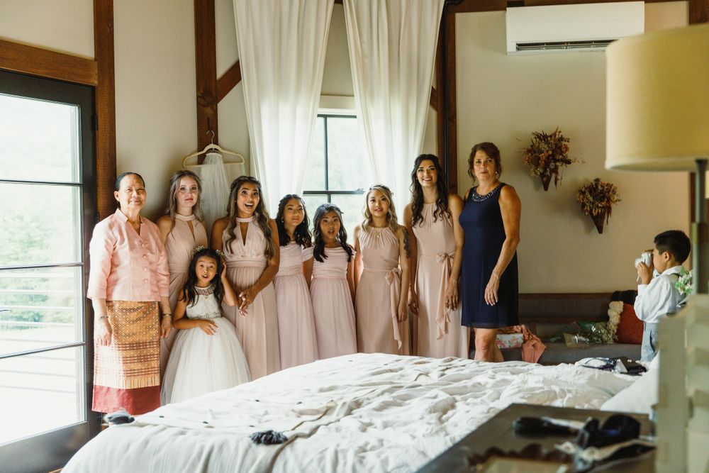 Wedding party gathered in rustic room with white curtains and wooden beams.
