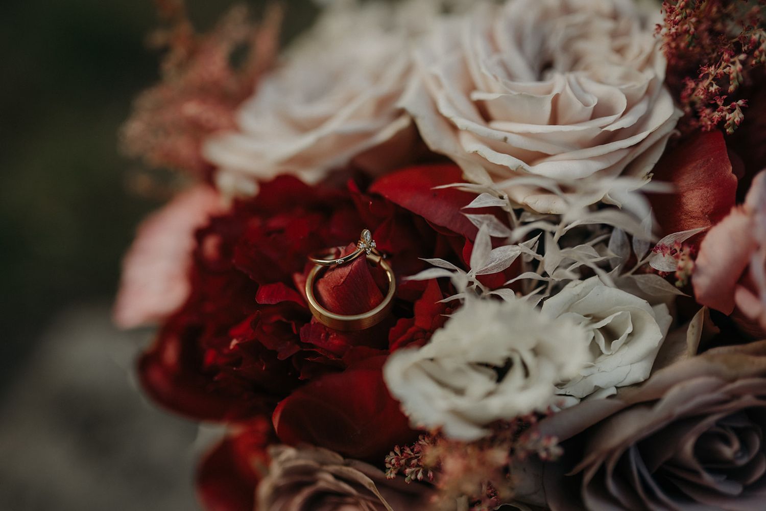Wedding ring nestled among pink and red roses in romantic floral arrangement.