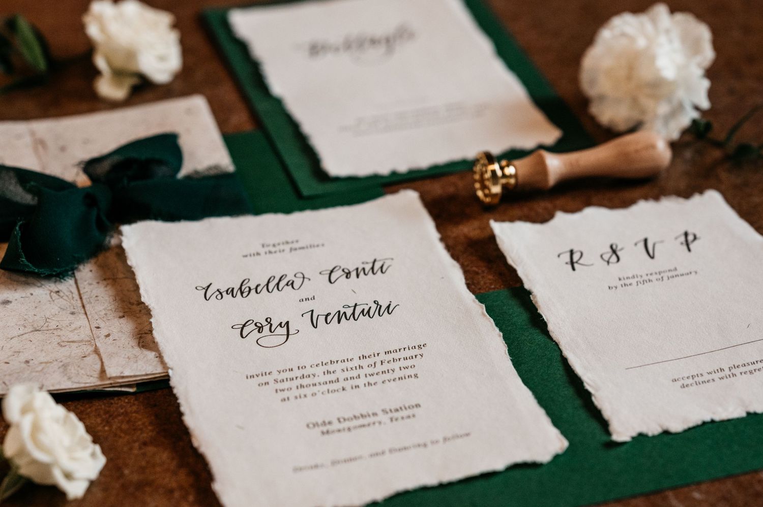 Wedding invitation suite with green accents and deckled edges on wooden surface.