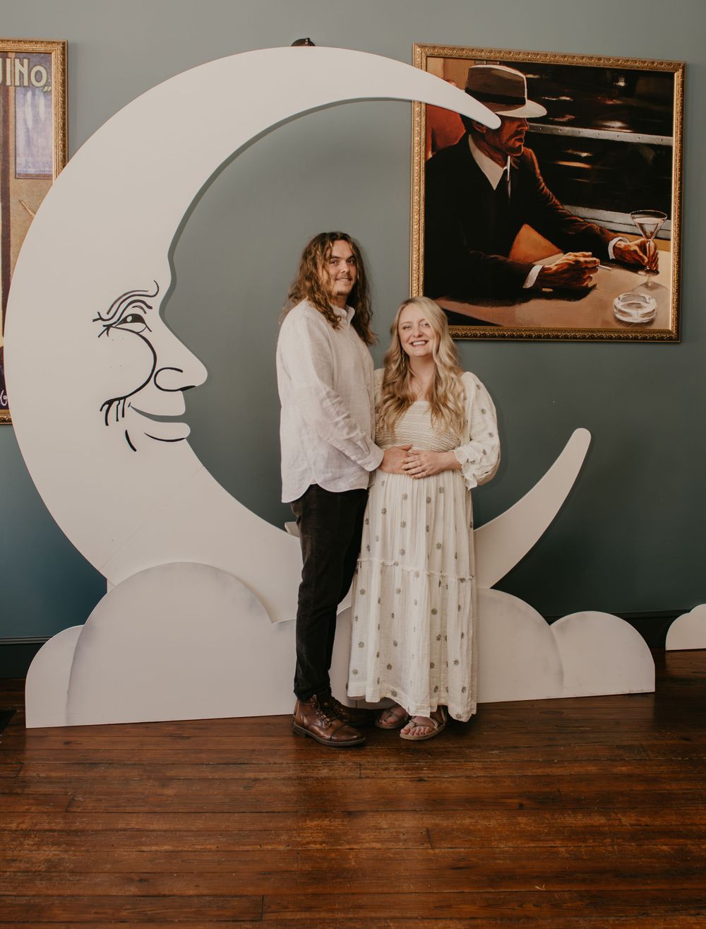 Expecting couple posing in front of large crescent moon prop at Baby Blatt baby shower celebration.