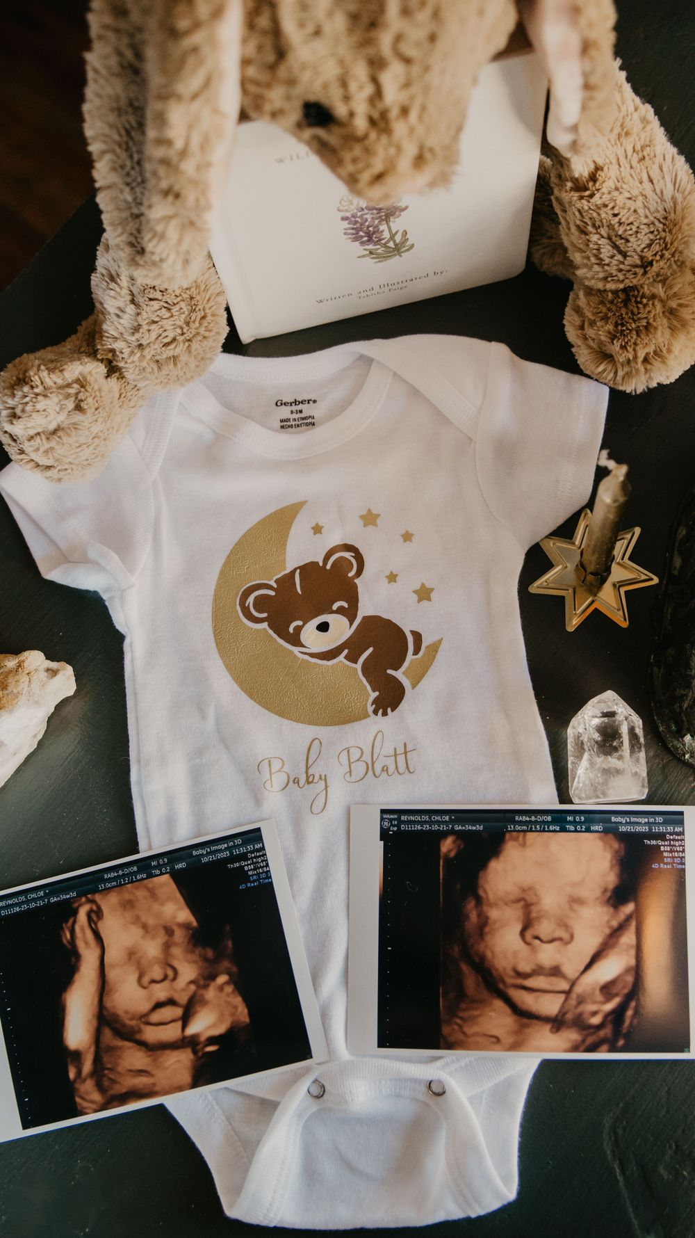 Baby Blatt onesie with sleeping bear on moon design displayed with 3D ultrasound photos and stuffed animals.