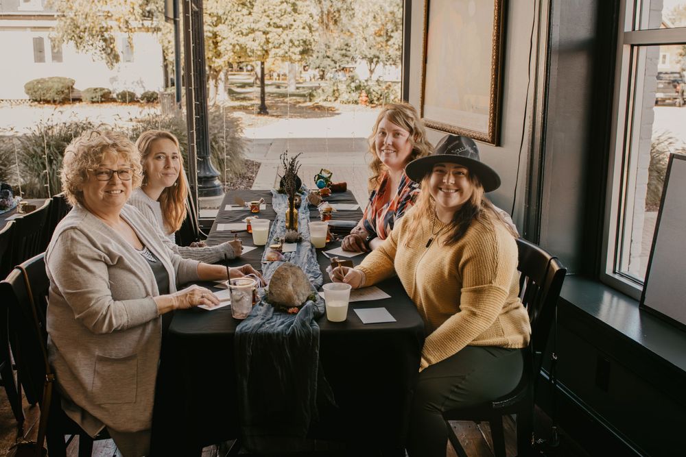 Group of five women smiling together at a restaurant table during a casual daytime gathering.