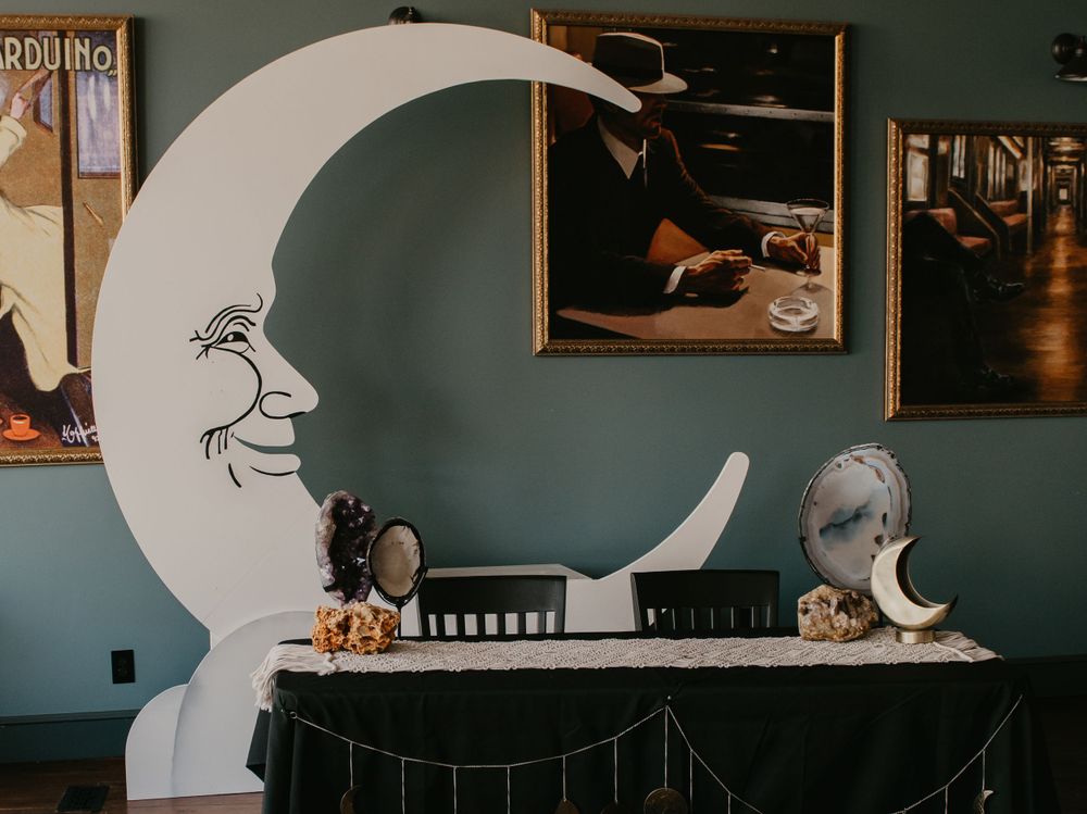 Decorative crescent moon photo booth prop on table with vintage art posters on wall.