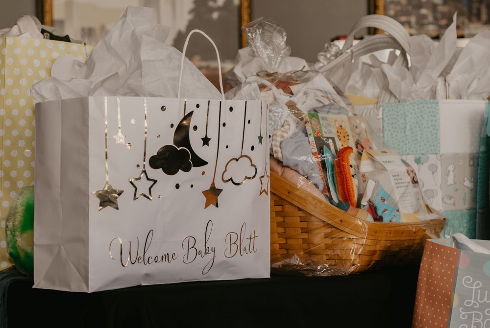 Welcome Baby Blatt gift bag with moon and stars design surrounded by wrapped presents and gift baskets at baby shower.