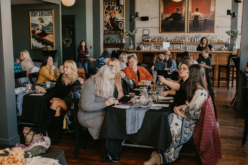 Guests seated at black tablecloth tables socializing at elegant baby shower brunch in restaurant venue.