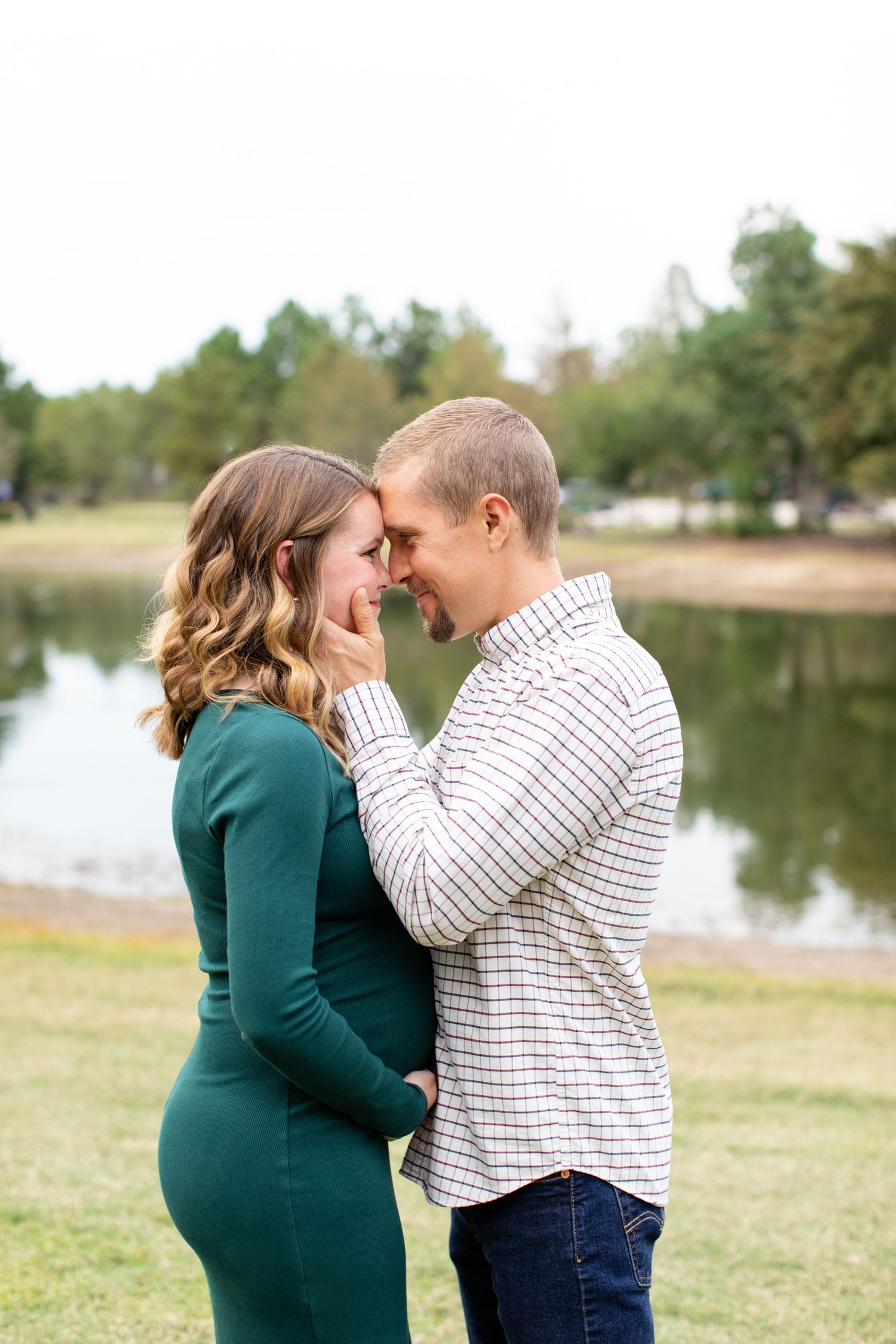 A couple shares an intimate moment by a pond on a cloudy day.