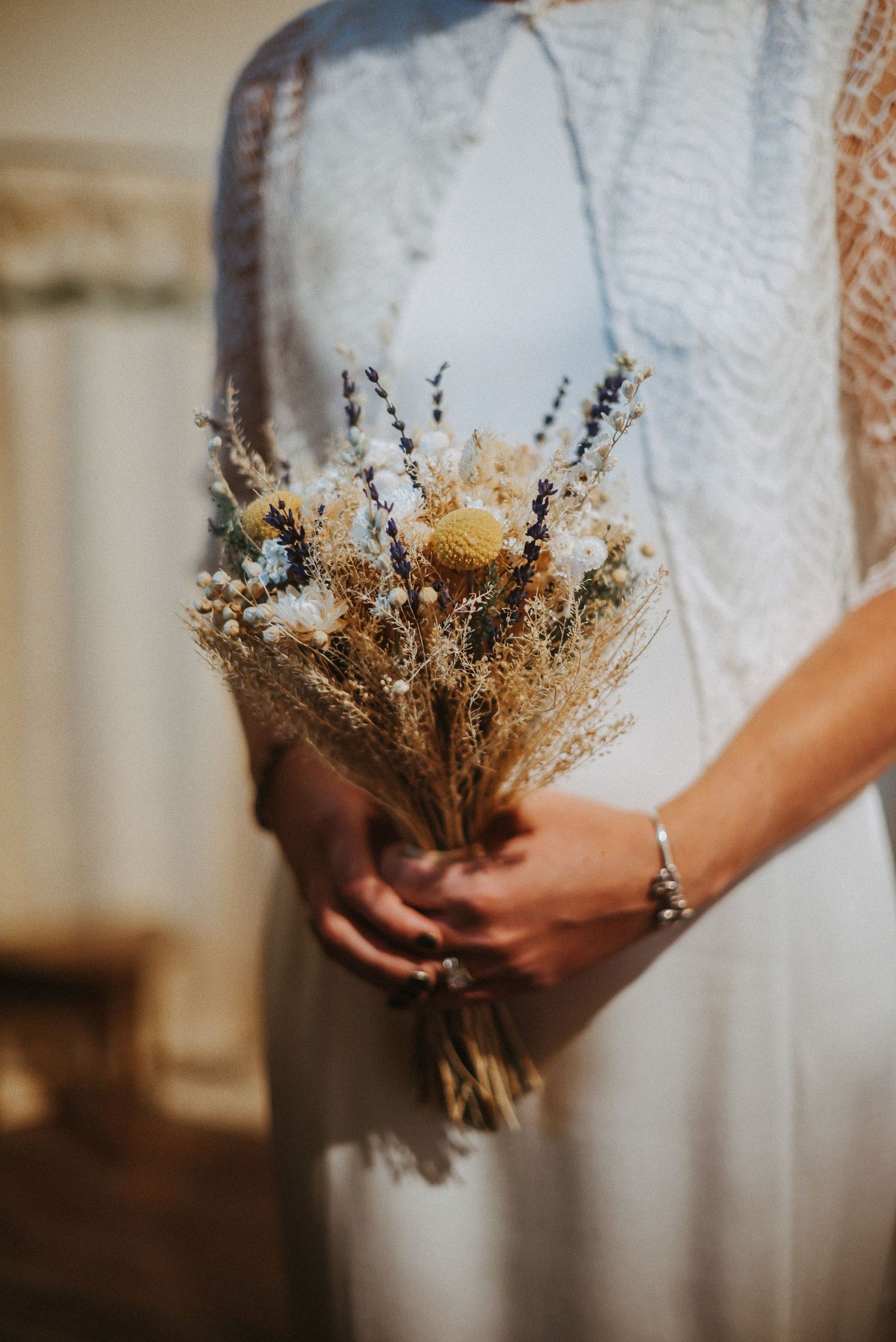 Rustic dried flower wedding bouquet held against white dress fabric.