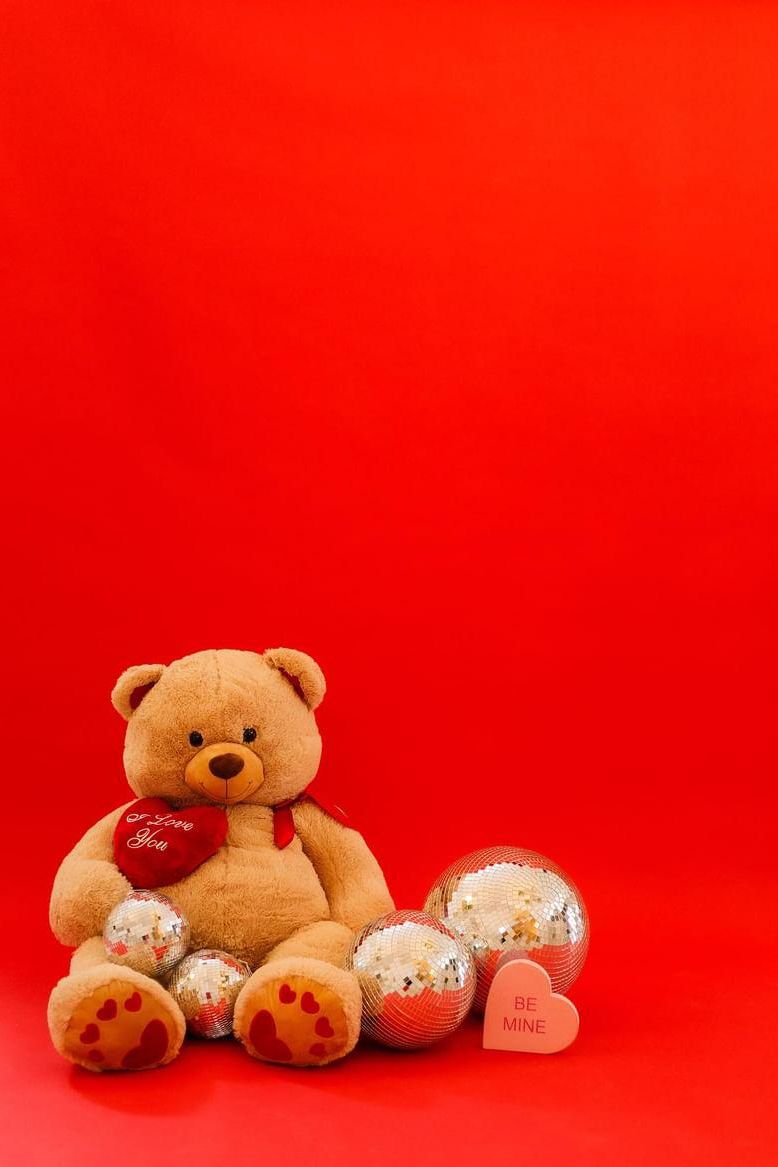 Teddy bear with heart and disco balls against vibrant red background for Valentine's Day.