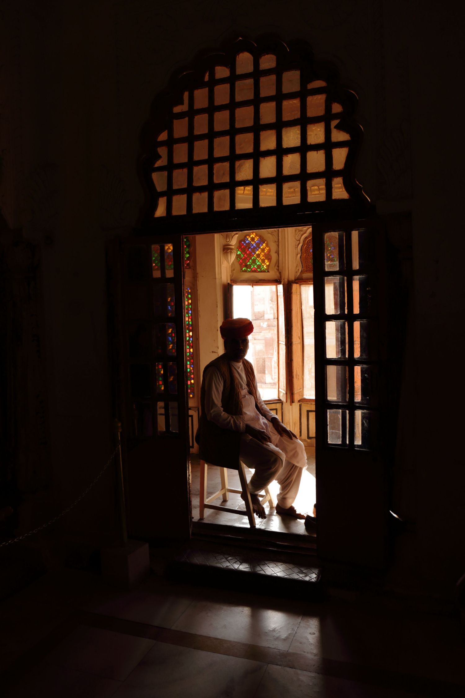 Silhouetted figure seen through traditional Indian latticed window during golden hour.
