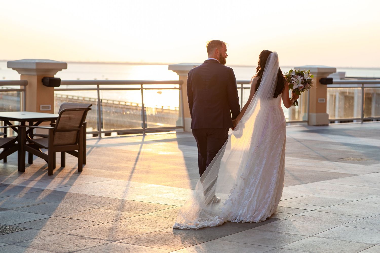 Silhouetted couple stands on a balcony overlooking the sunset during their wedding day.