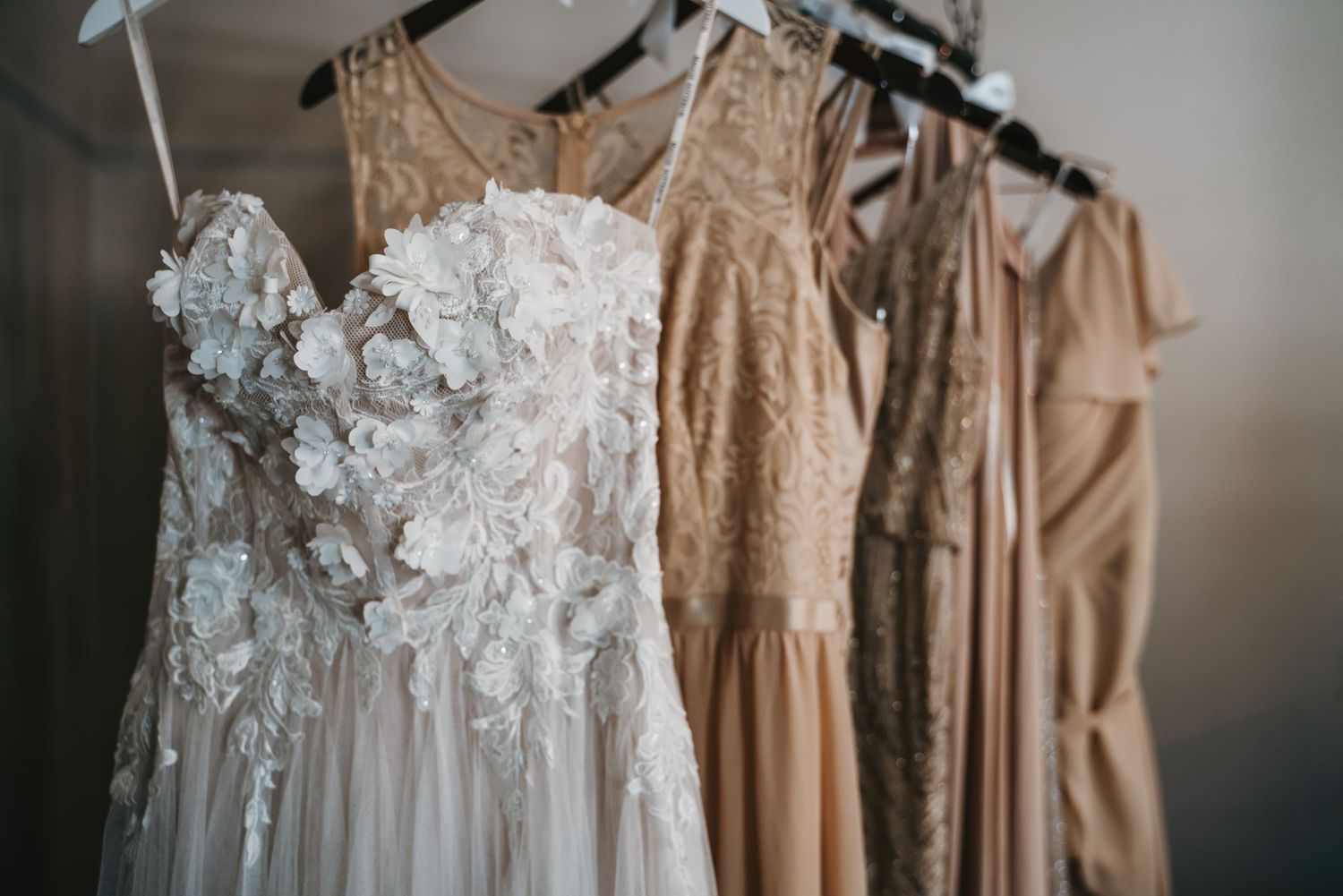 Wedding dresses in soft neutral tones displayed on hangers showing intricate lace details.