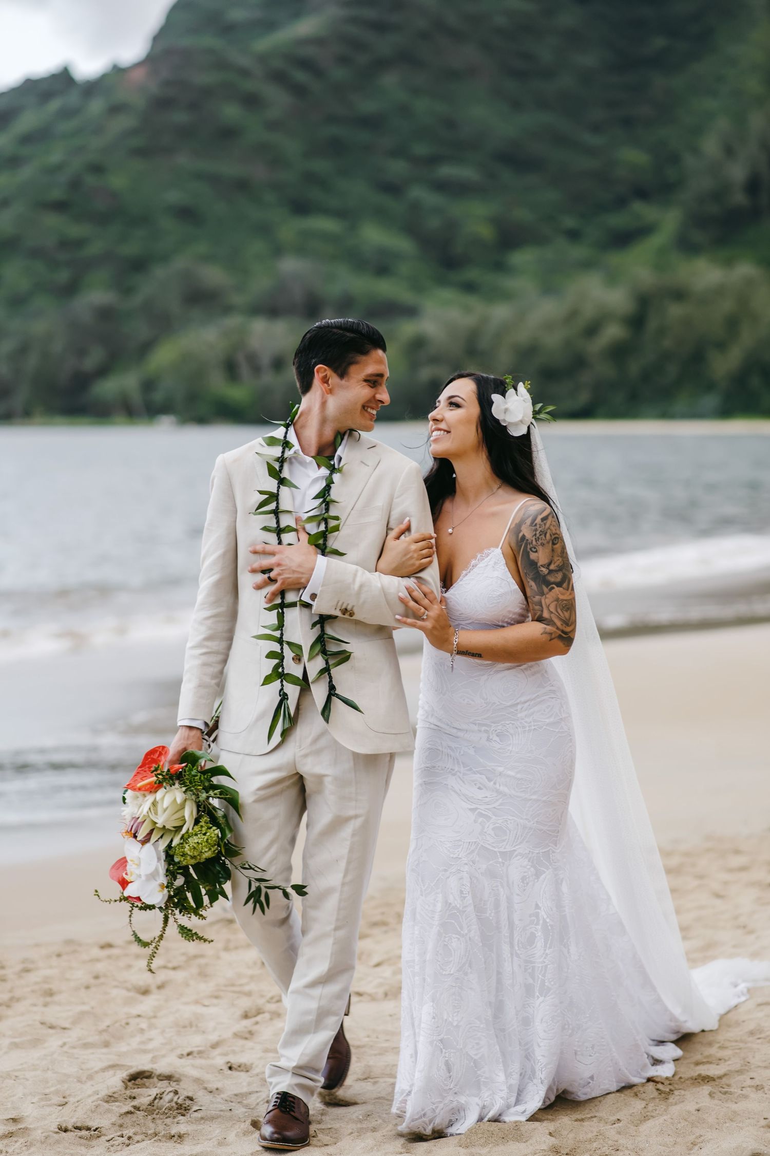 A romantic beach wedding couple in light attire share a joyful moment on a tropical shore.