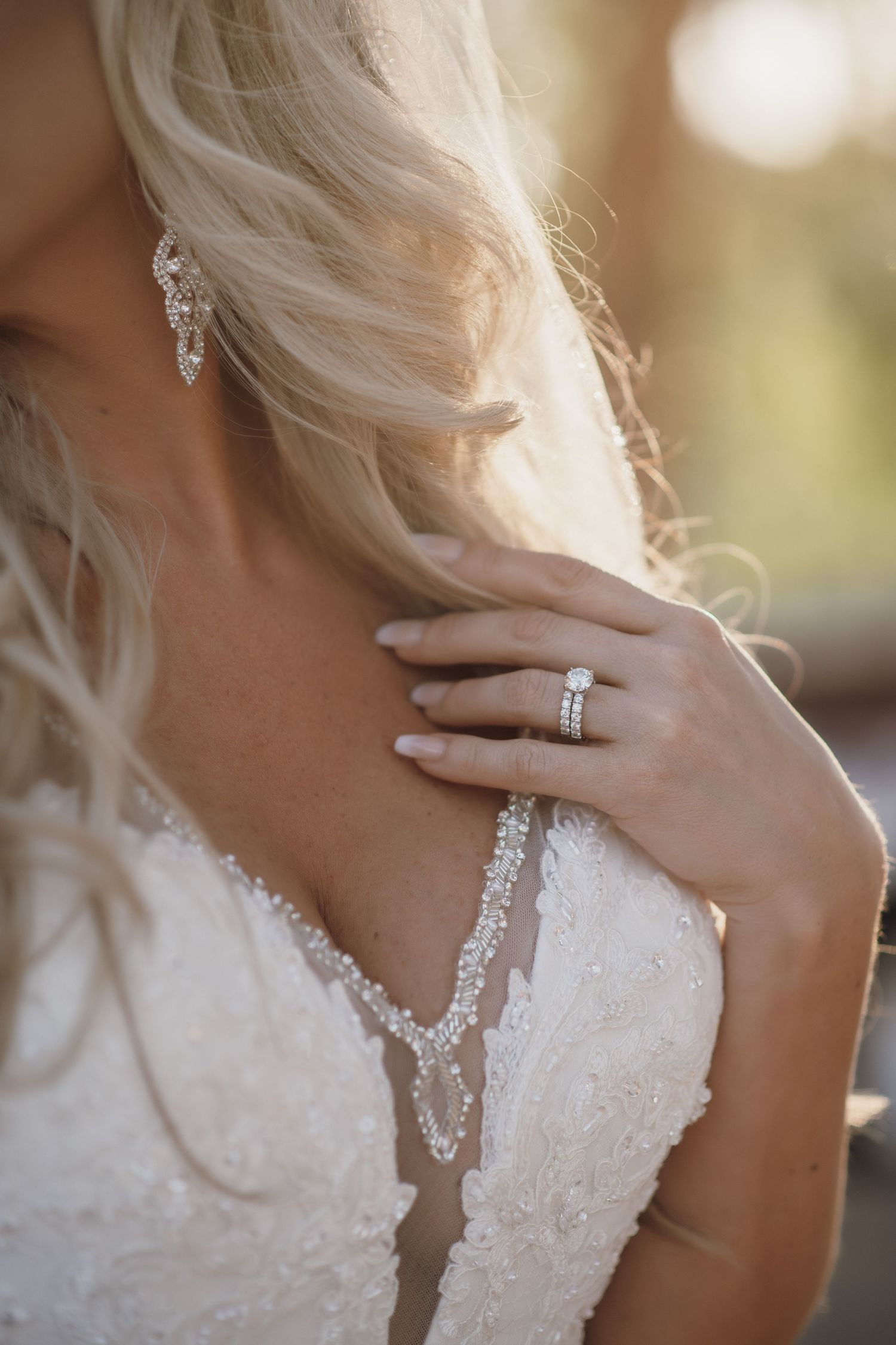 Close-up of a bride's detailed lace dress and diamond engagement ring with flowing blonde hair.