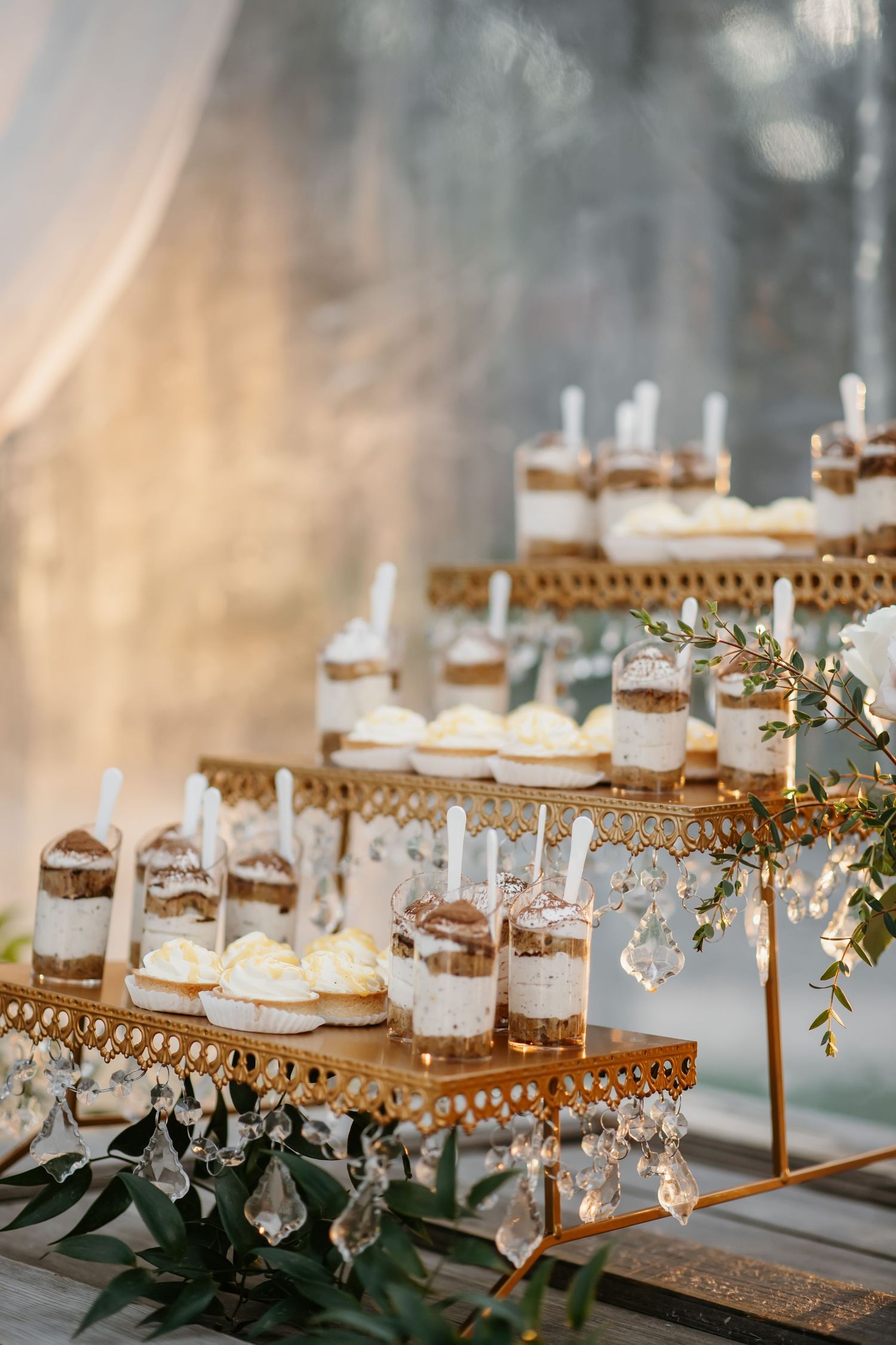 Elegant tiered dessert display with glass chandelier decorations and miniature desserts in jars.