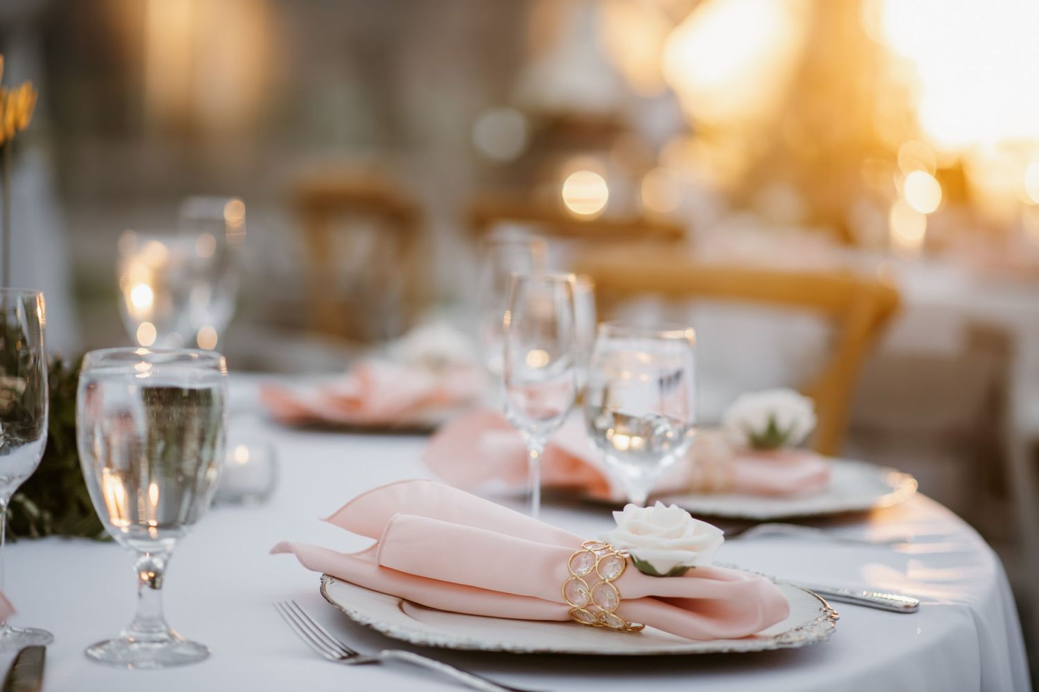 Wedding reception table setting with pink napkin and wine glasses in soft lighting.