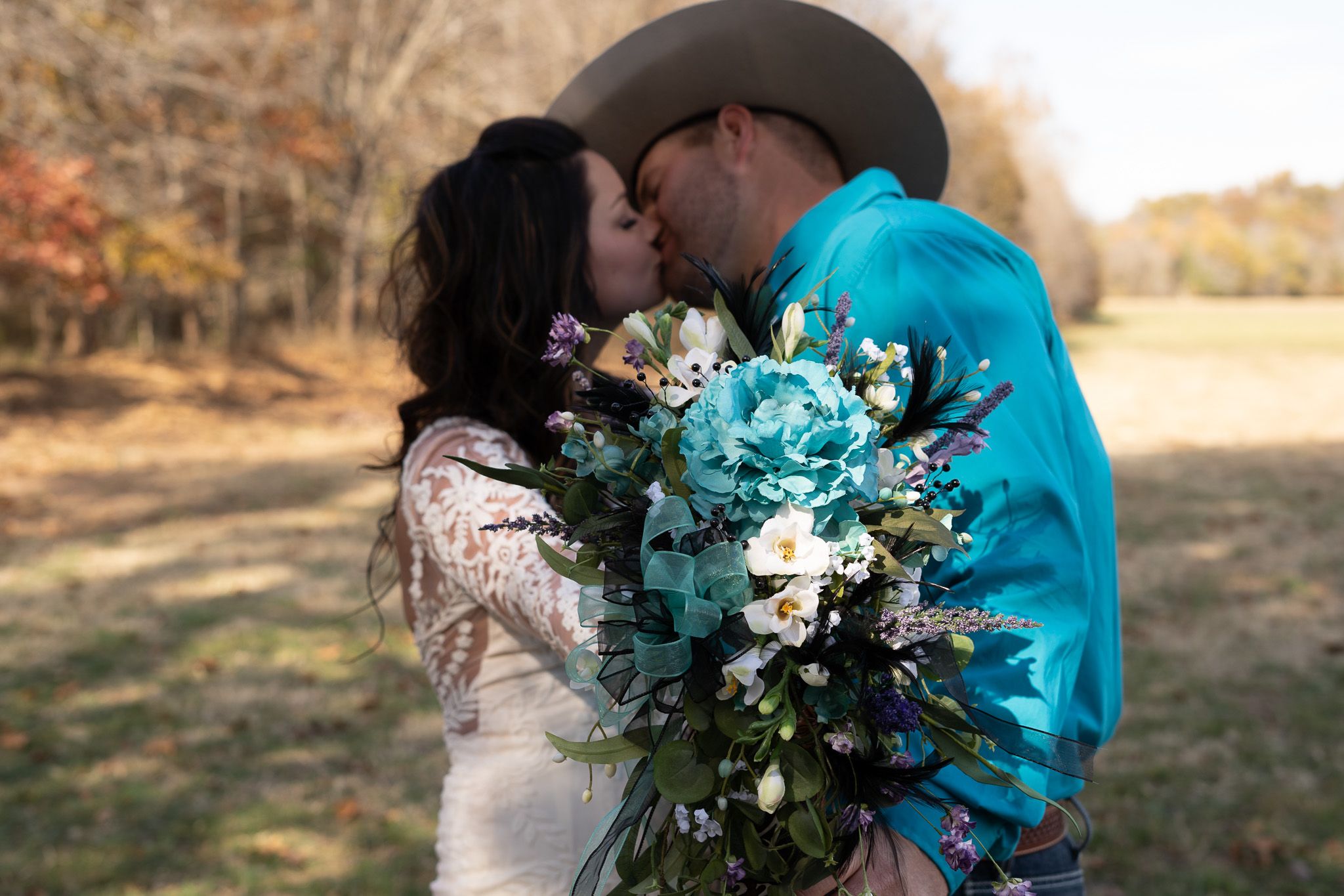 A bride holds her flowers to camera as she kisses groom