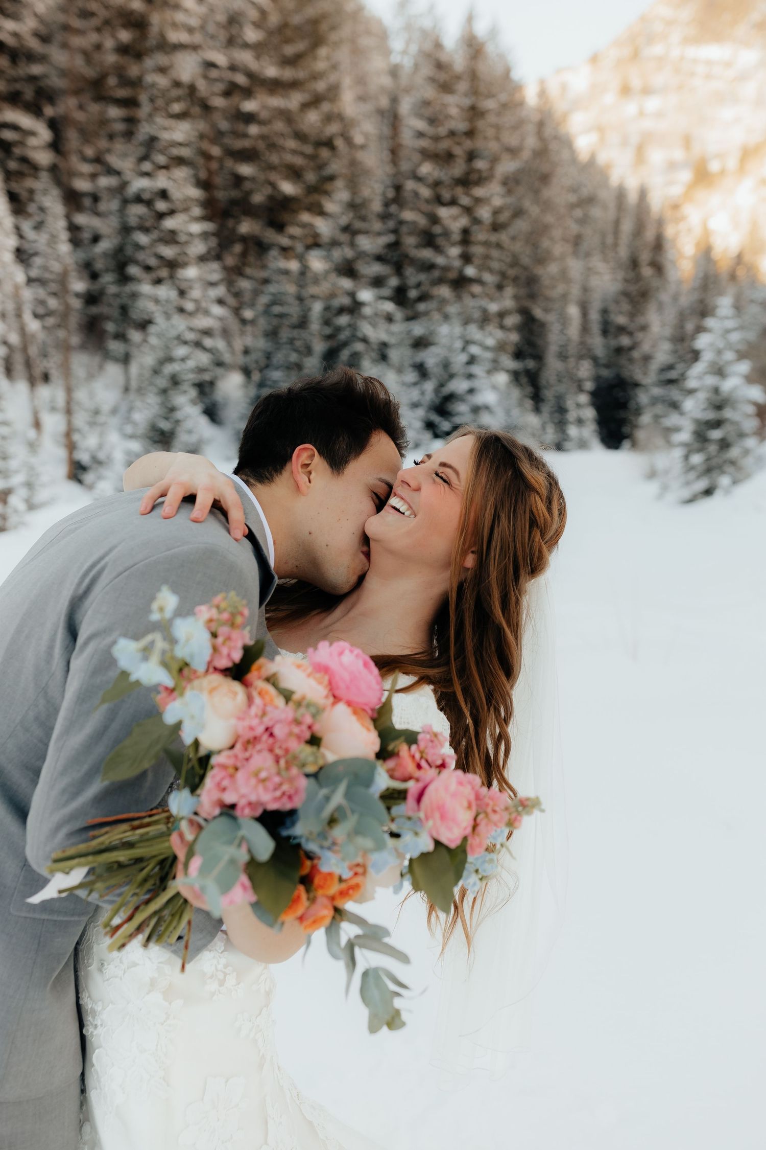 Bride laughs as groom kisses neck in winter mountains
