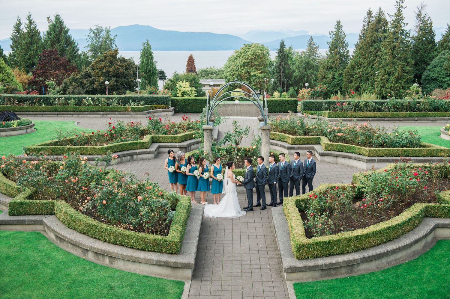Formal garden ceremony setup with symmetrical pathways and manicured hedges surrounded by evergreens.