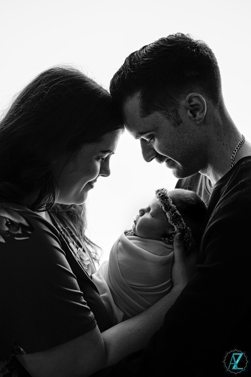 Black and white silhouette of parents looking down at their swaddled newborn.