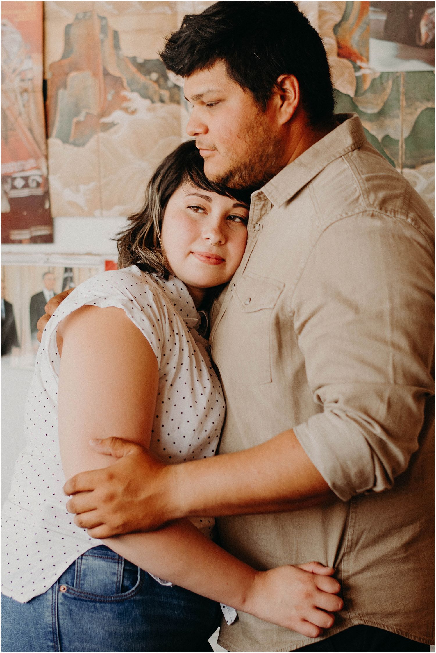 Couple embracing tenderly against wall with decorative artwork in background.