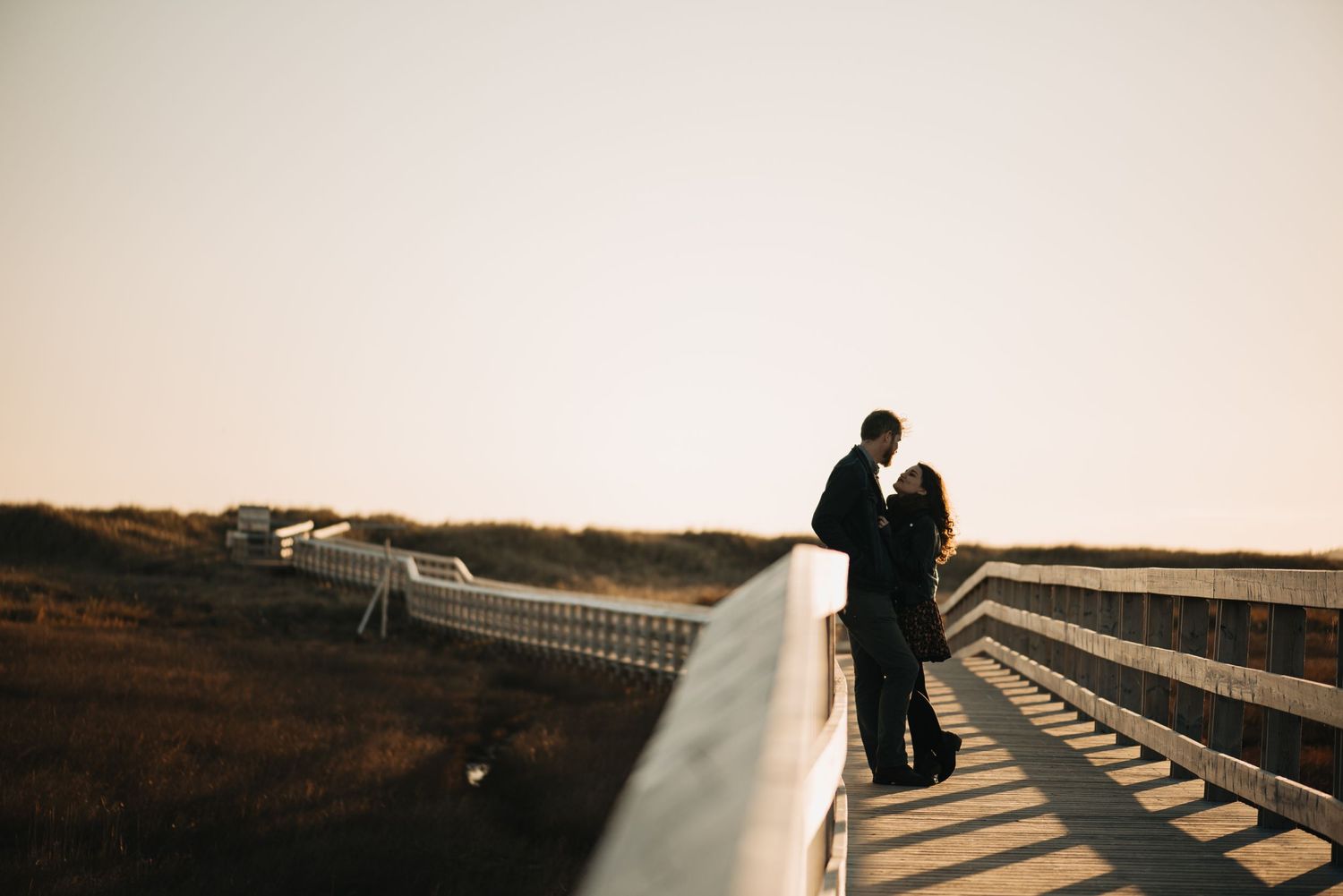 A silhouetted couple share a romantic moment on a bridge at sunset.