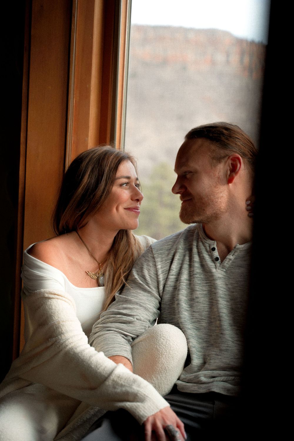 Cozy indoor portrait of couple sharing tender moment by window with natural lighting.