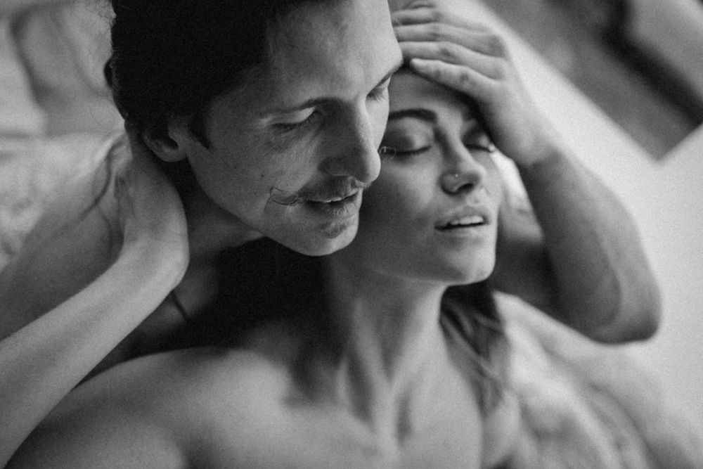 An intimate black and white photograph capturing a tender romantic moment between two people in soft lighting.