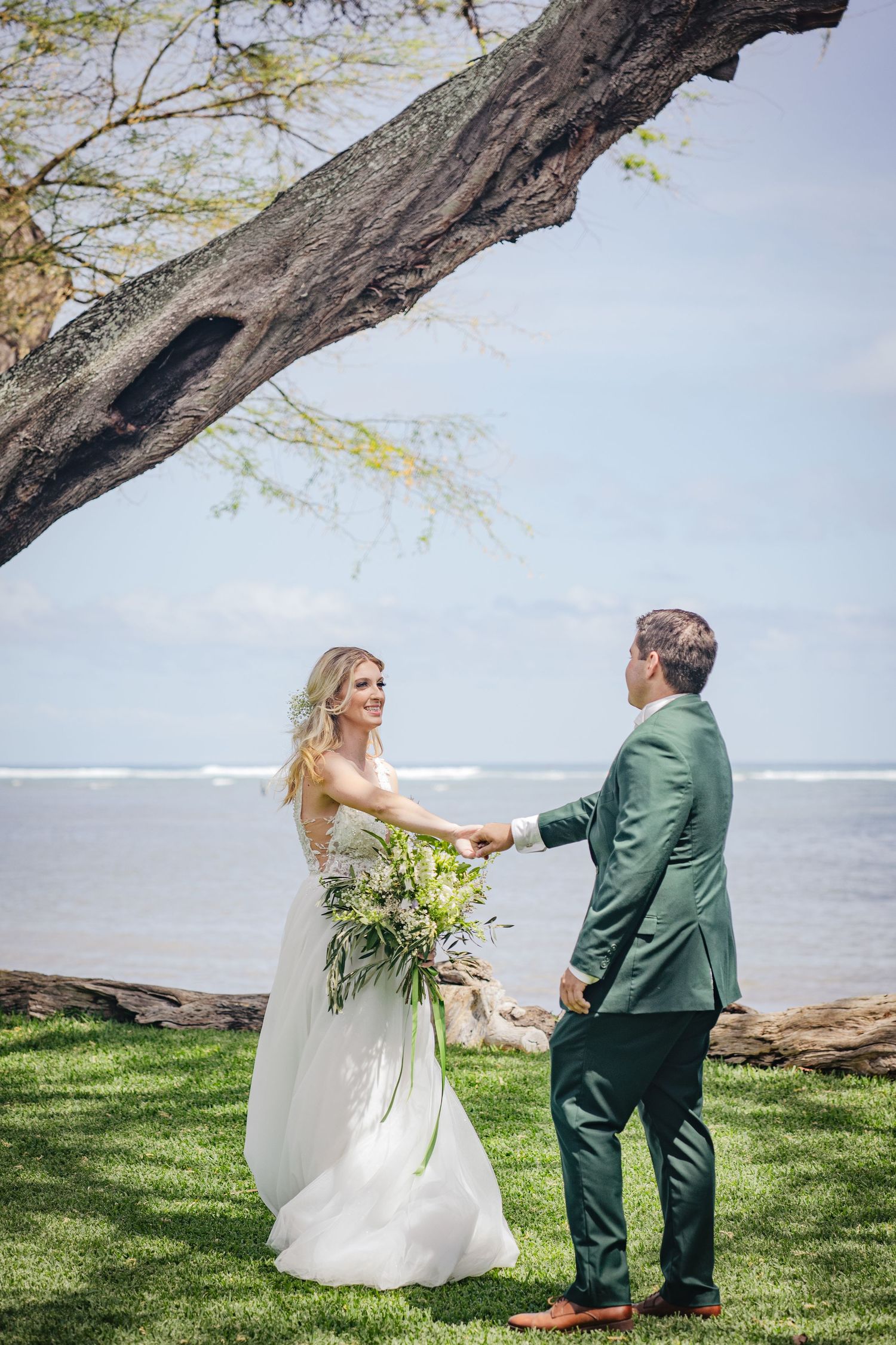 A seaside wedding portrait beneath a dramatic tree branch overlooking the ocean.