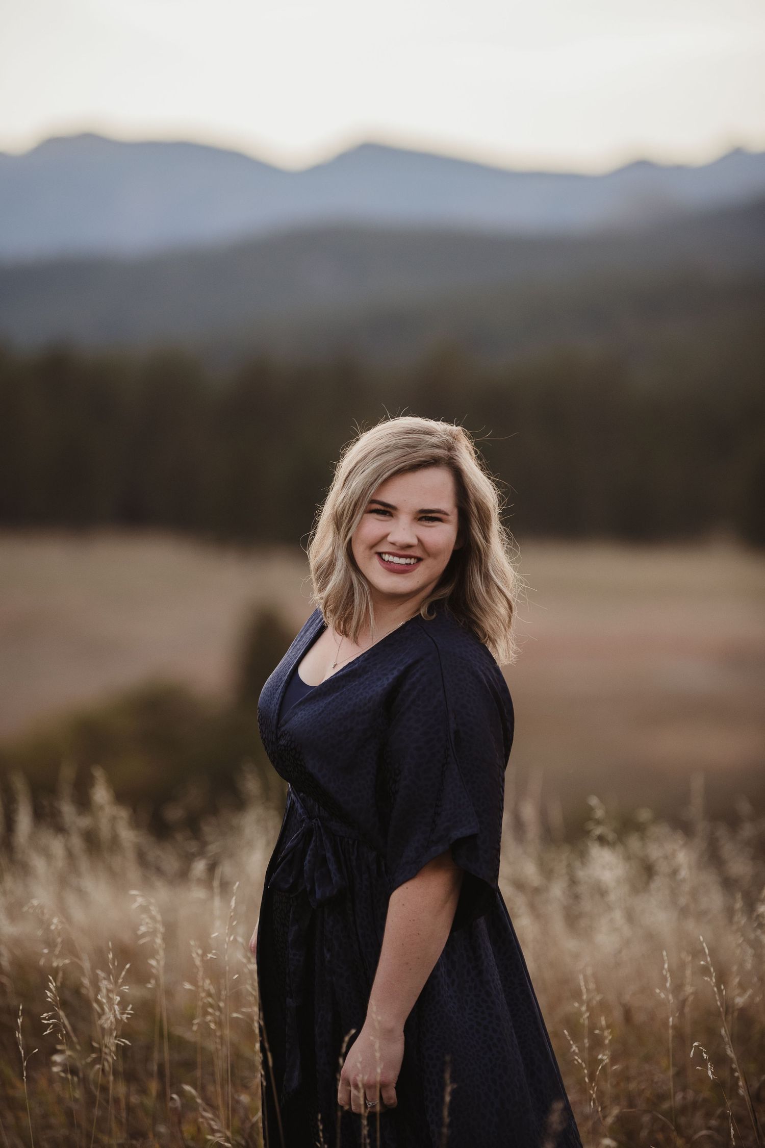 Portrait session in field with mountain backdrop at golden hour.
