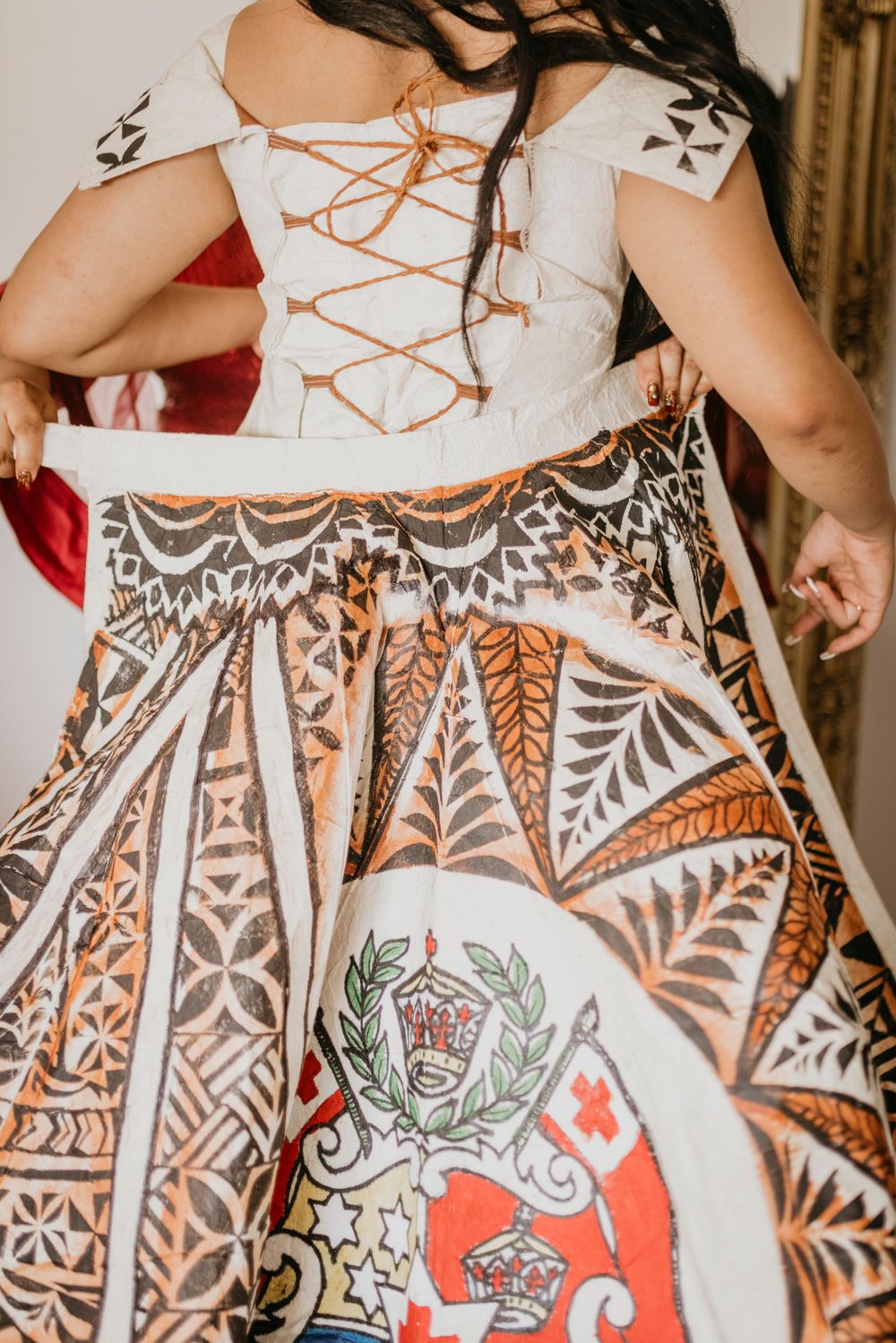 Beautiful dress train being put on graduate with details of Tongan cultural symbols