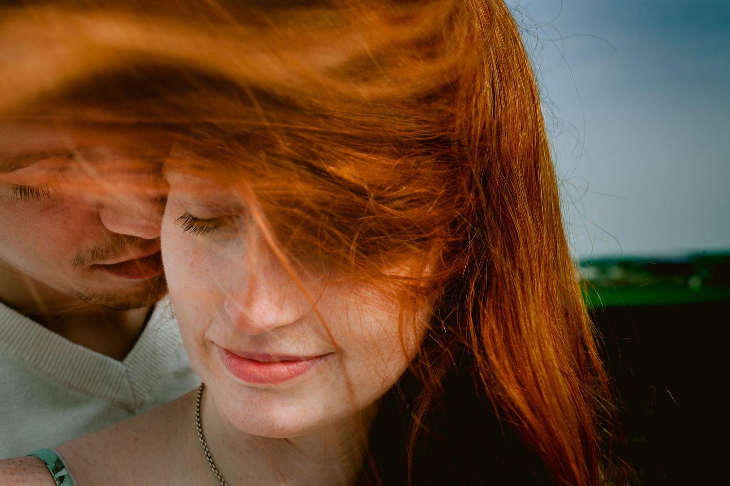 An intimate close-up portrait with sunlit red hair in the foreground.