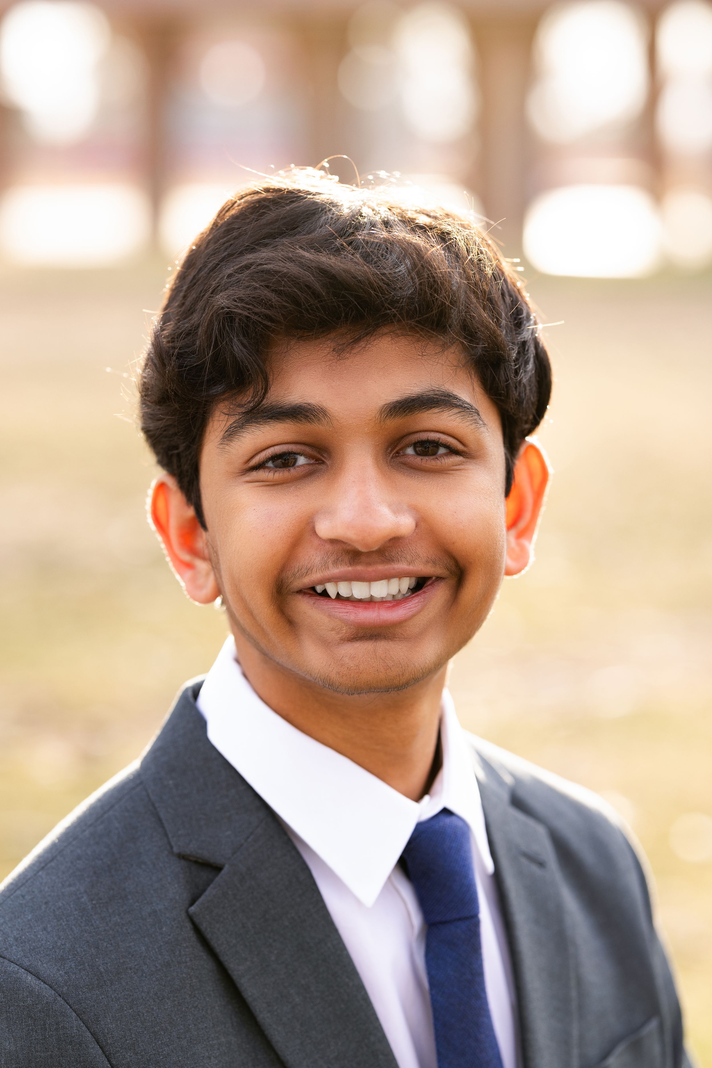 Professional headshot of someone in dark suit and blue tie with friendly smile.