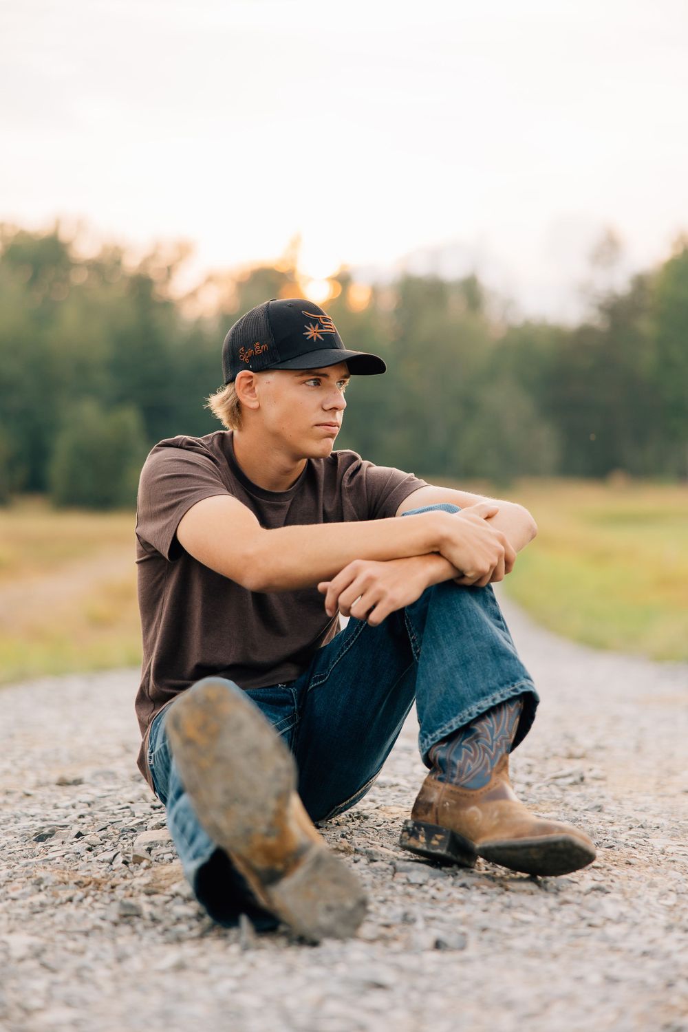 Person in casual wear sitting thoughtfully on gravel path at dusk.