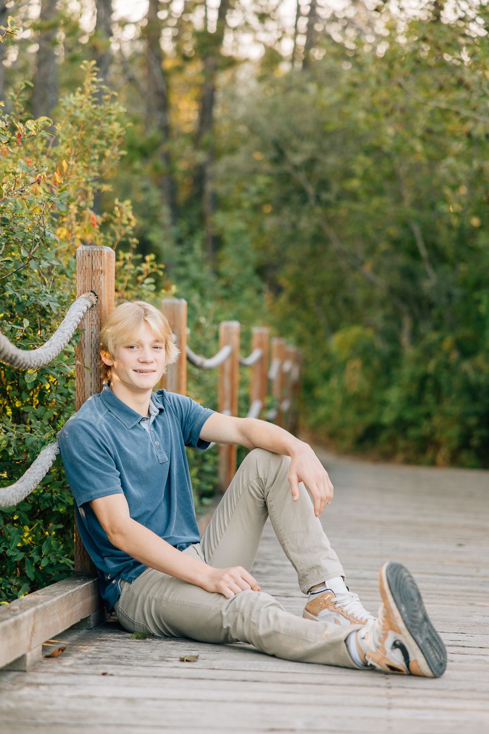 Person in blue polo relaxing on wooden boardwalk surrounded by greenery.
